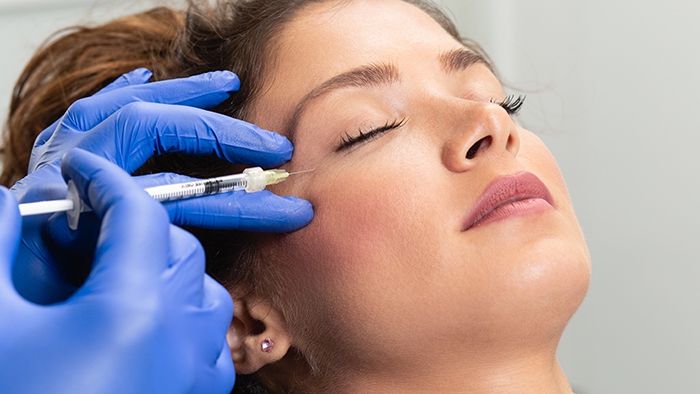 gloved hands use a syringe to inject near a woman's closed eyes