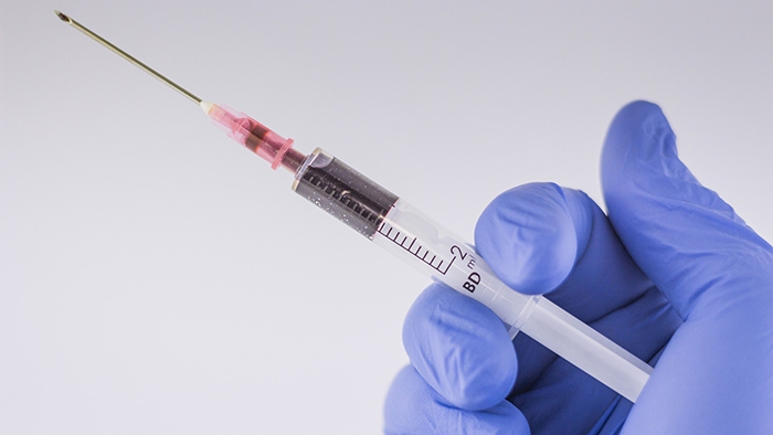 Needle with red liquid held in gloved hand